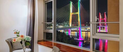 A room with a large window overlooking a brightly lit bridge at night.