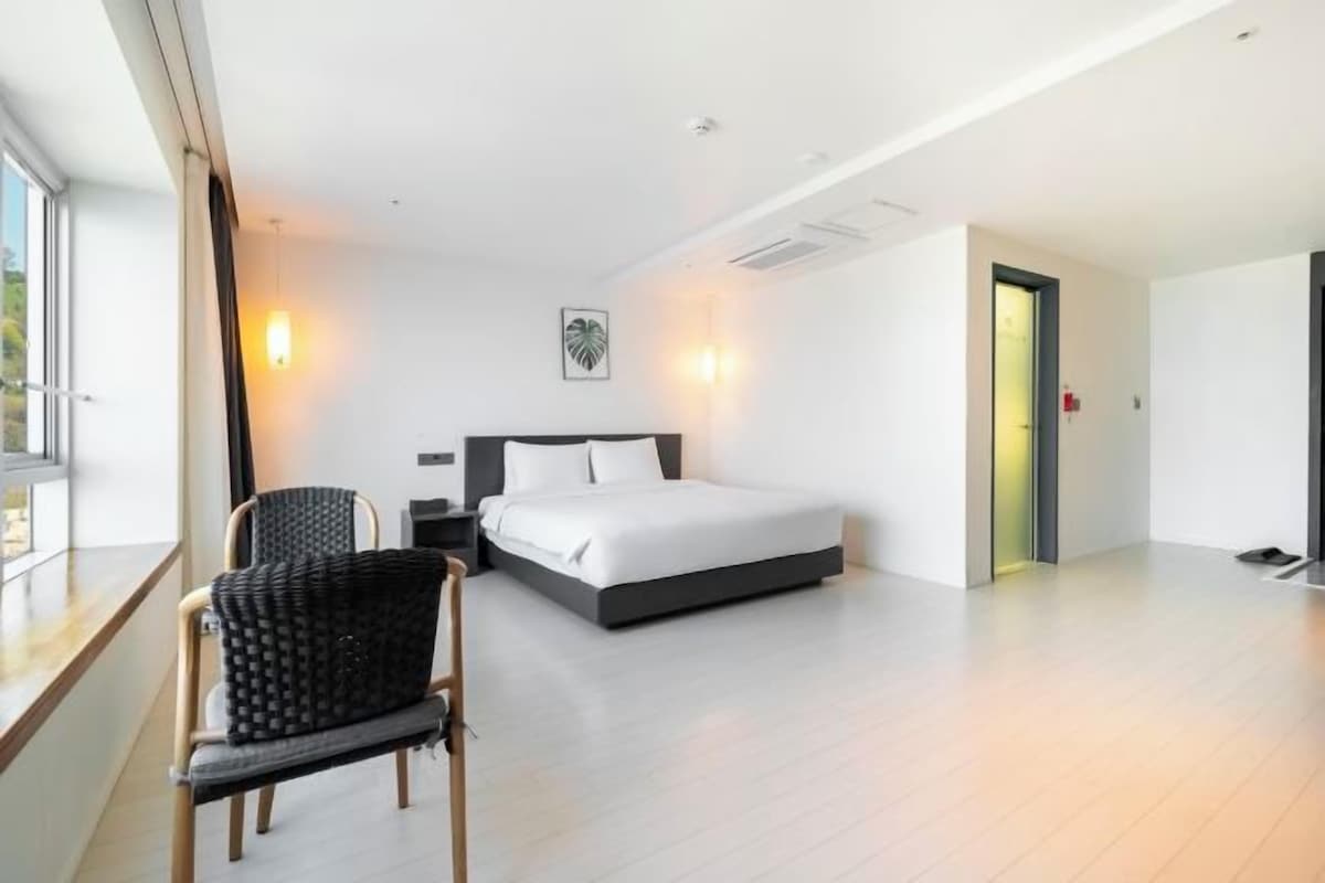 Ett modernt hotellrum med en stor säng, en stol och ett nattduksbord.