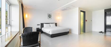 A modern hotel room with a large bed, a seating area with a chair, and a view through the window.