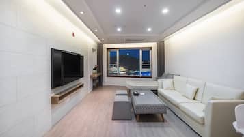 A modern living room with a flat-screen TV, a sofa, a coffee table, and a window with a view of a cityscape at night.