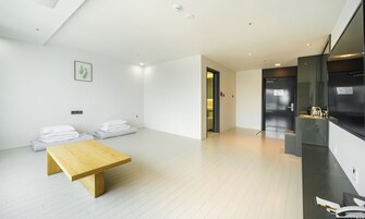 A modern, minimalist room with a wooden table, white bedding, and a black refrigerator.