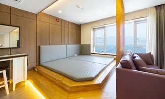Habitación de hotel moderna con una cama grande, un escritorio pequeño, un sofá y una ventana con vista al mar.