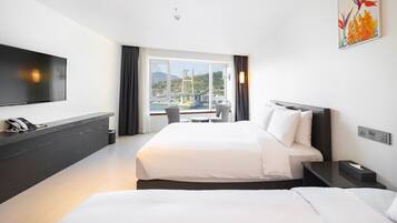 A hotel room with a bed, bedside tables, a TV, a phone, and a window with a view of a bridge and greenery.