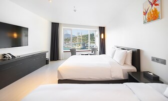 A hotel room with a bed, bedside tables, a TV, a phone, and a window with a view of a bridge and greenery.