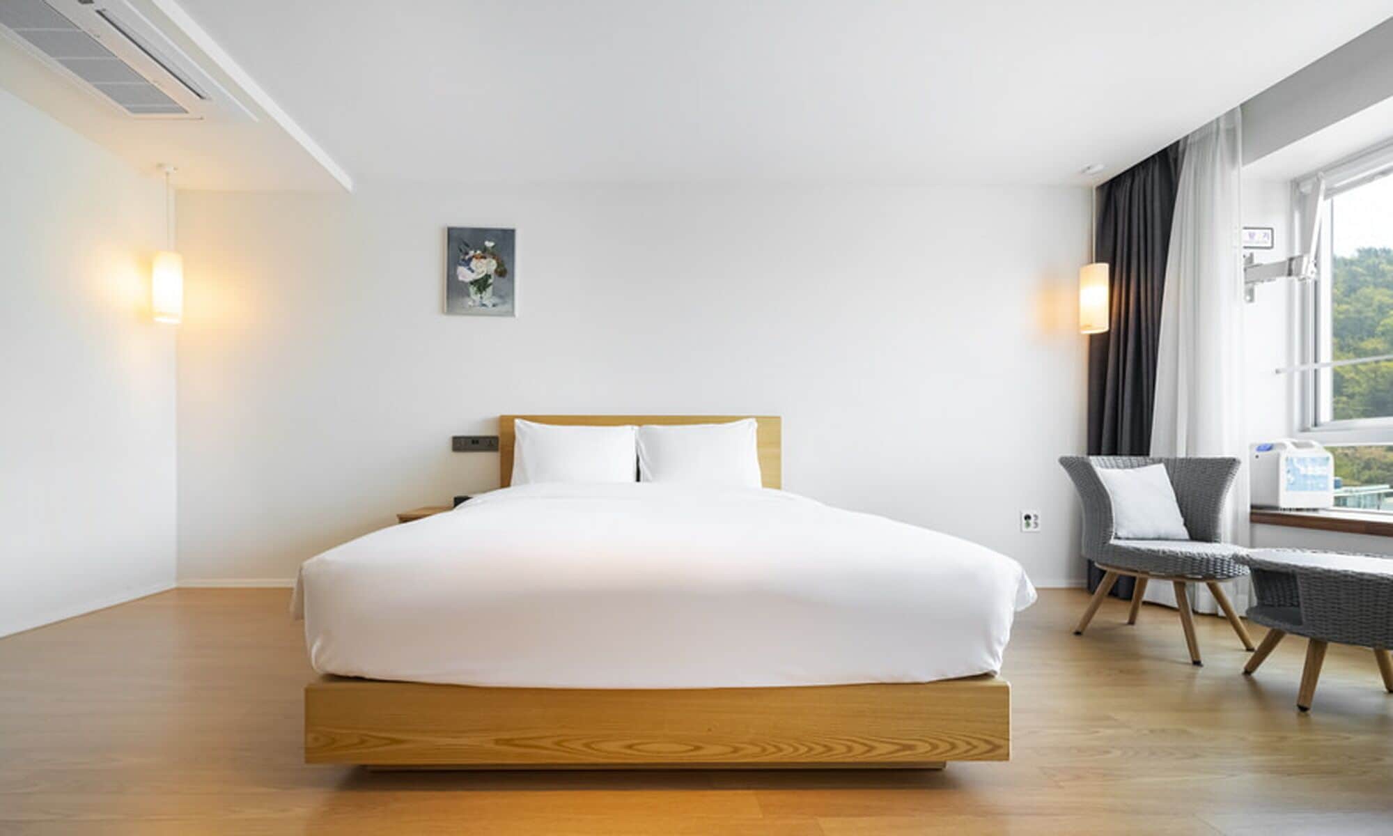 A modern hotel room with a wooden bed, a small table, a chair, and a window with curtains.
