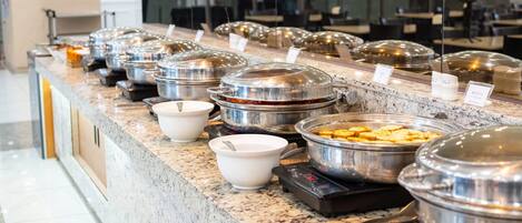 Ein reichhaltiges Buffet mit verschiedenen Speisen in abgedeckten Behältern, einer Kaffeemaschine und einem Wasserspender.