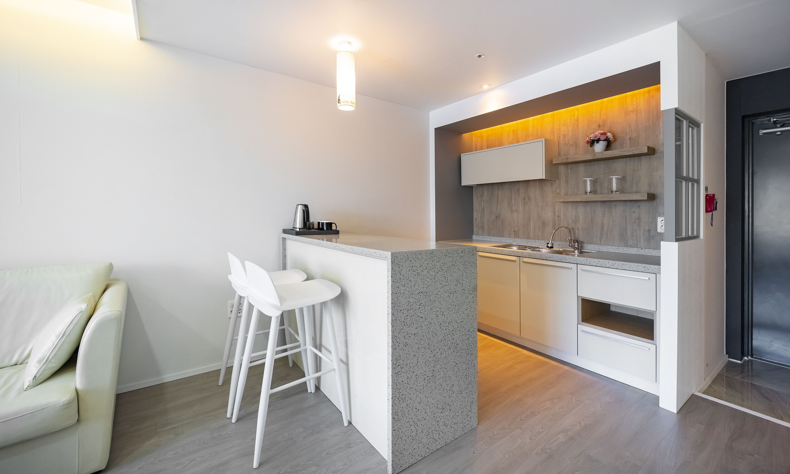 A modern kitchen with a bar area, white bar stools, and a built-in oven.