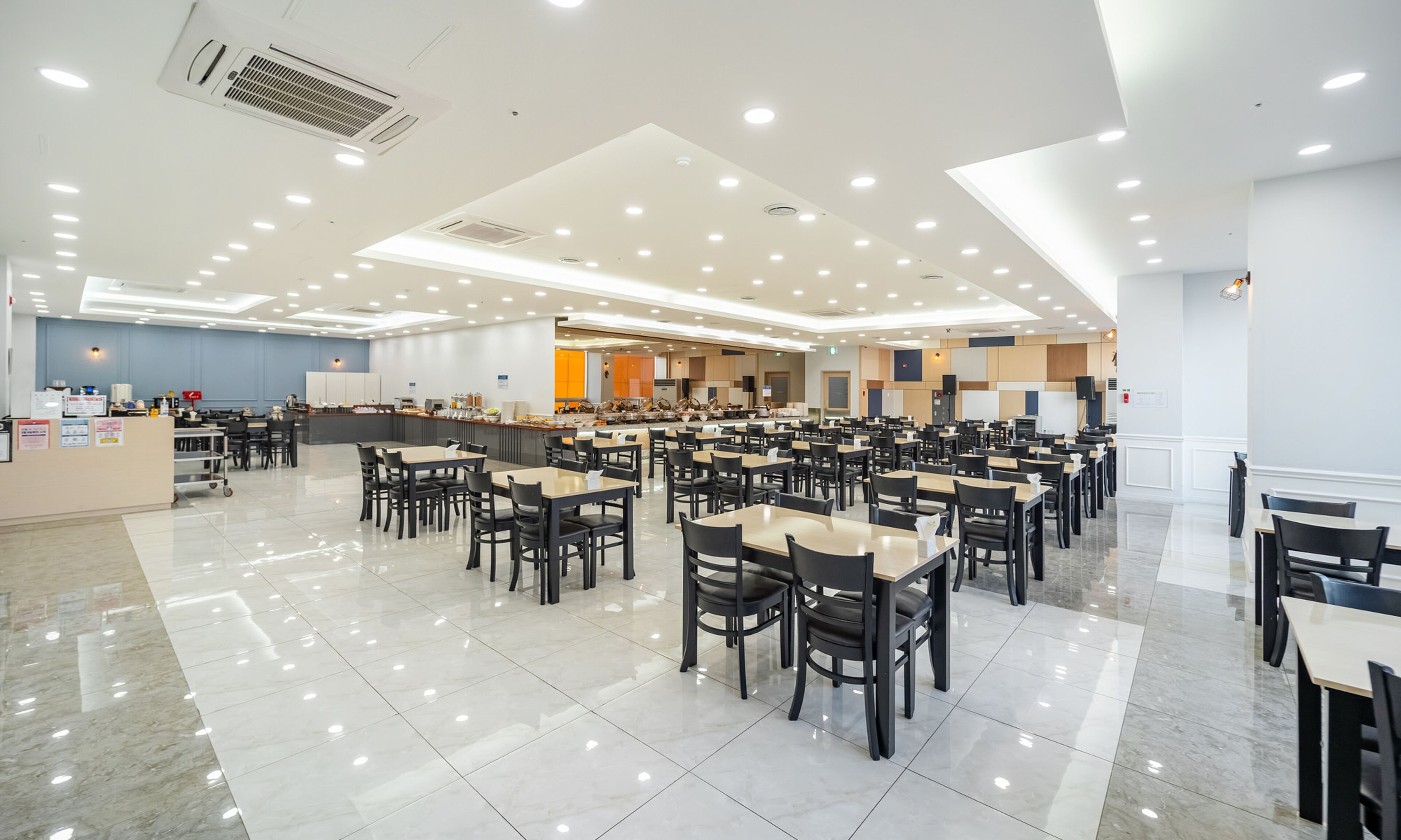 Un comedor amplio con varias mesas y sillas, una estación central de servicio y un techo luminoso con iluminación empotrada.