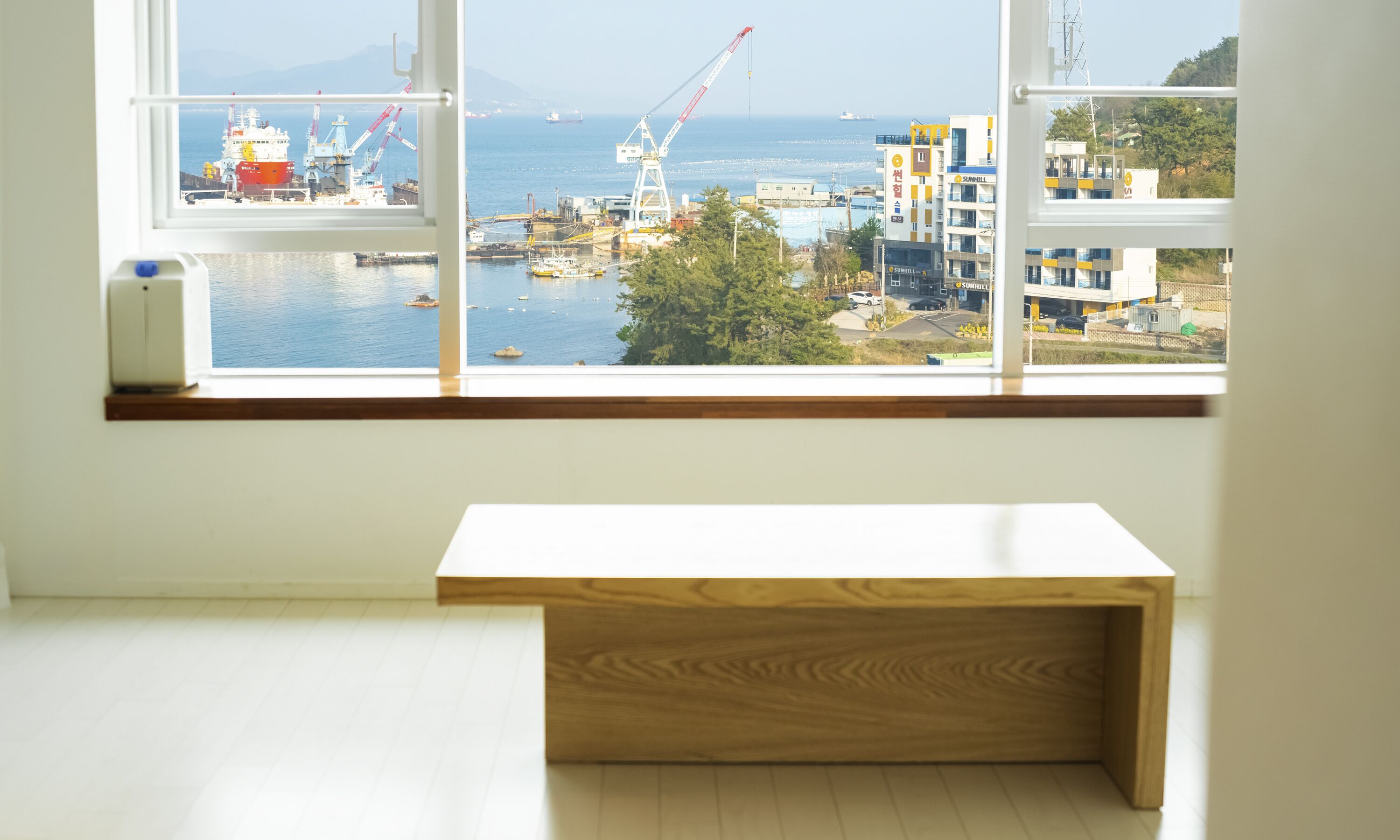 Ein Zimmer mit großem Fenster mit Blick auf einen Hafen, in dem Schiffe und Kräne zu sehen sind.