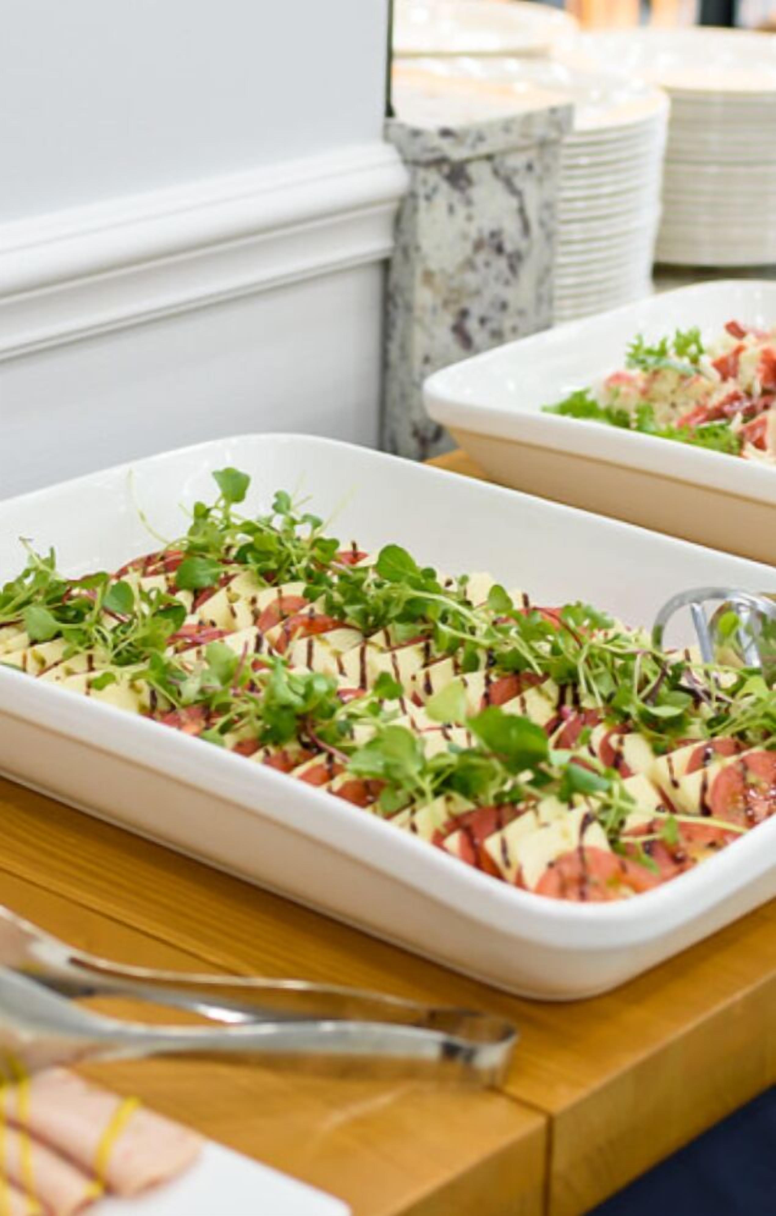 A white rectangular dish with a layered salad on a wooden table.