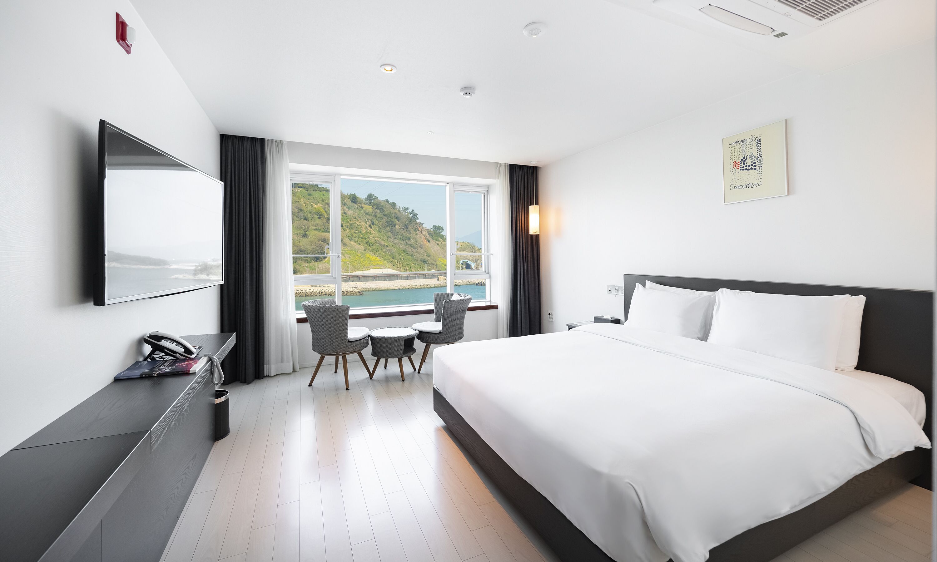 Une chambre d’hôtel avec un lit, un bureau et une chaise, une télévision et une fenêtre donnant sur la mer.