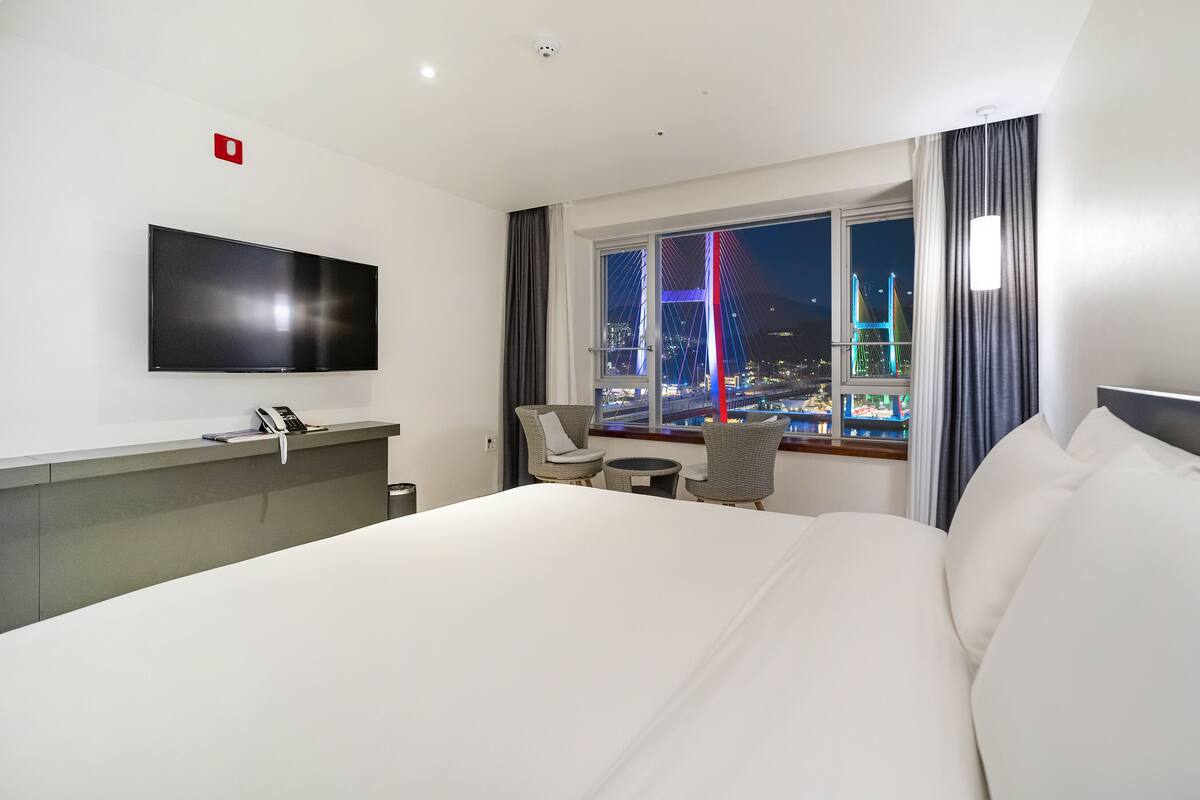 Hotellihuone, jossa on sänky, kirjoituspöytä, jossa on puhelin, tuoli ja televisio.