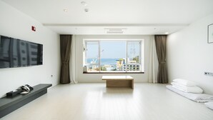 Habitación de hotel moderna con un ventanal grande, un televisor de pantalla plana, una mesita de centro de madera y una cama con ropa de cama blanca.