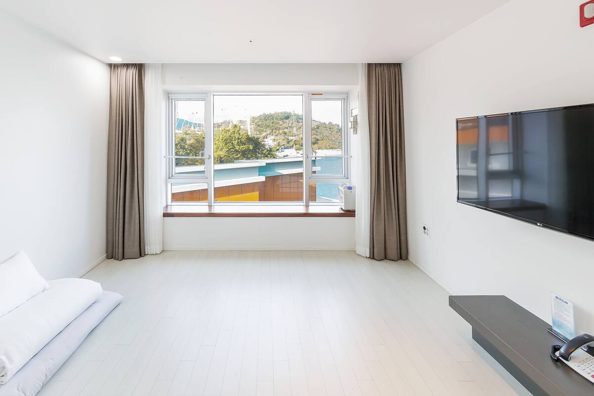 Hotellihuone, jossa on suuri ikkuna, sänky, televisio ja työpöytä, jossa on puhelin.