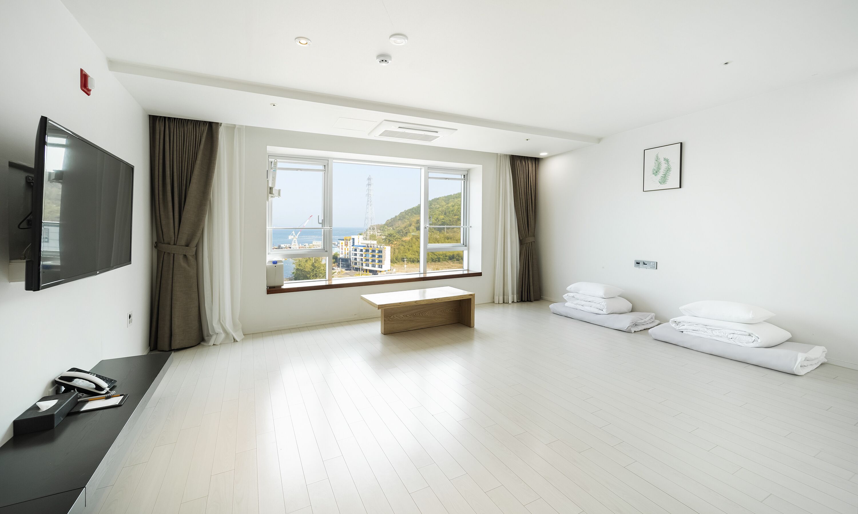 A spacious room with a large window, a flat-screen TV, a desk with a telephone, and neatly folded towels.