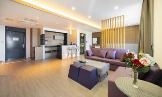 A modern living room with a sofa, ottoman, and coffee table, a kitchen area with bar stools, and a door leading to a bathroom.
