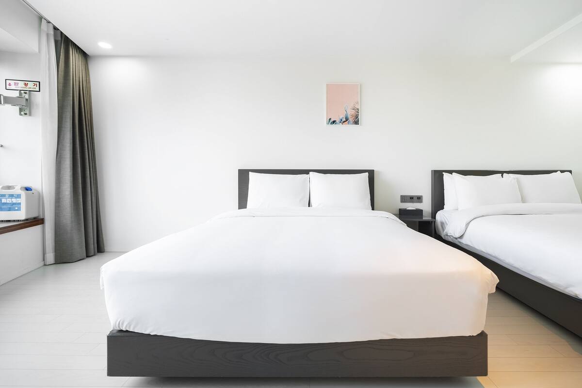 Hotellihuone, jossa on kaksi sänkyä, yöpöytä, seinään asennettu ilmastointilaite ja taulu.