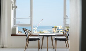 A room with two chairs facing a large window overlooking a construction site and a body of water. - Hotel Haven (Yeosu)