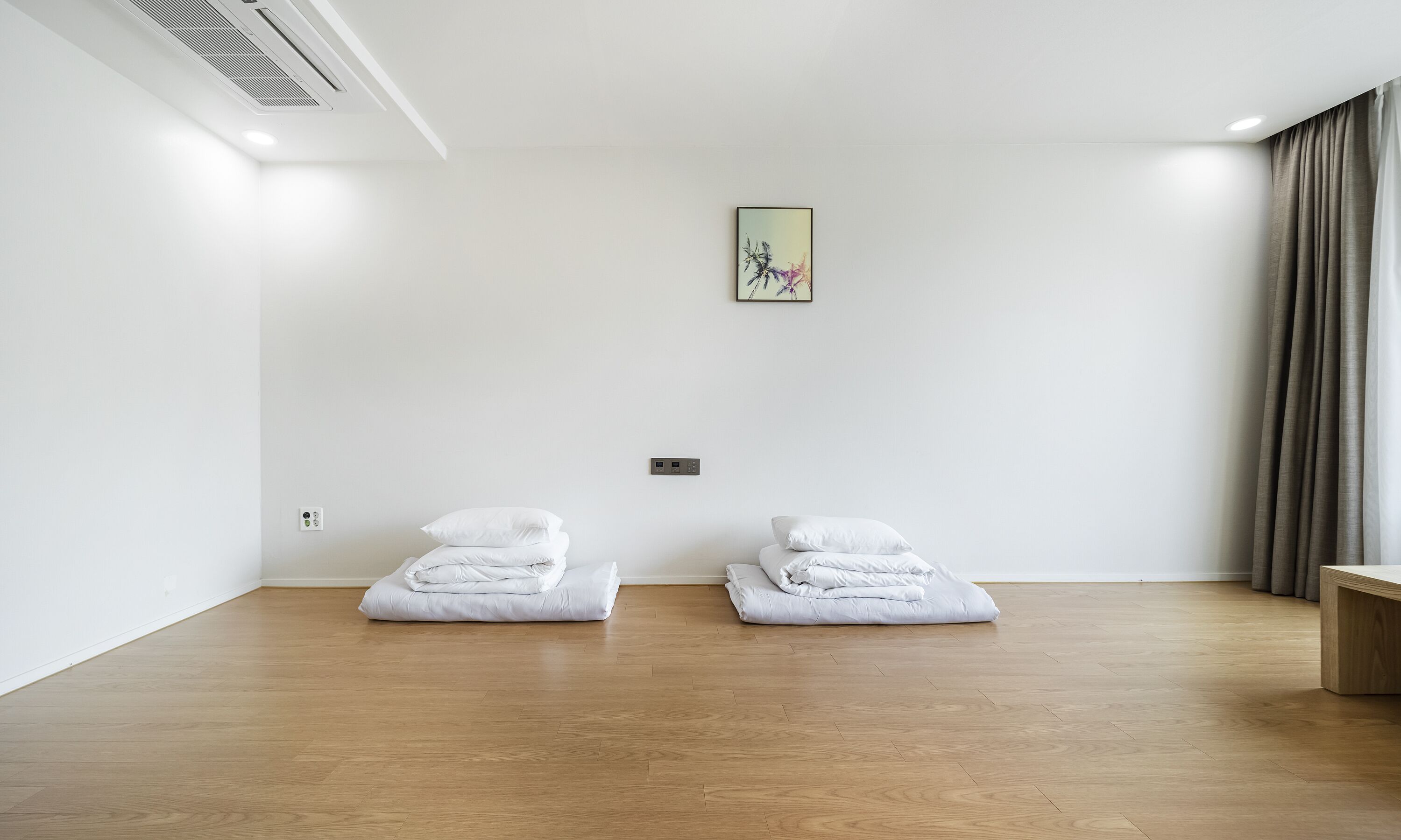 Habitación de hotel con piso de madera, dos camas blancas con almohadas, un cuadro en la pared y una ventana con cortinas.