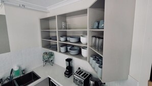 A kitchen with white cabinets, a built-in shelf unit, a sink, and various kitchen appliances. - Landing Pads Brunswick - Hostel (Brunswick)