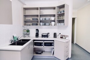 A compact kitchen with a sink, two microwaves, a toaster, and a coffee maker. - Landing Pads Brunswick - Hostel (Brunswick)