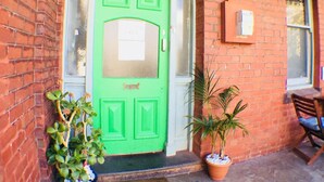 A green door with a window above it, a potted plant to the left, and a bench to the right. - Landing Pads Brunswick - Hostel (Brunswick)