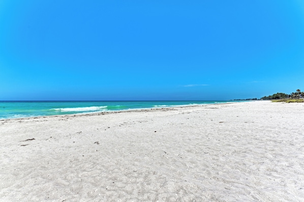 A wide sandy beach with clear blue water and a clear sky.