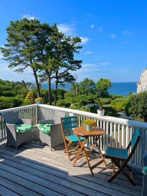 A wooden deck with wicker furniture and a small table, overlooking a coastal landscape with trees and a house. - Ocean Views, 100 steps to The Cliff House!  Minutes to Ogunquit, Perkins Cove, Beaches! (York)