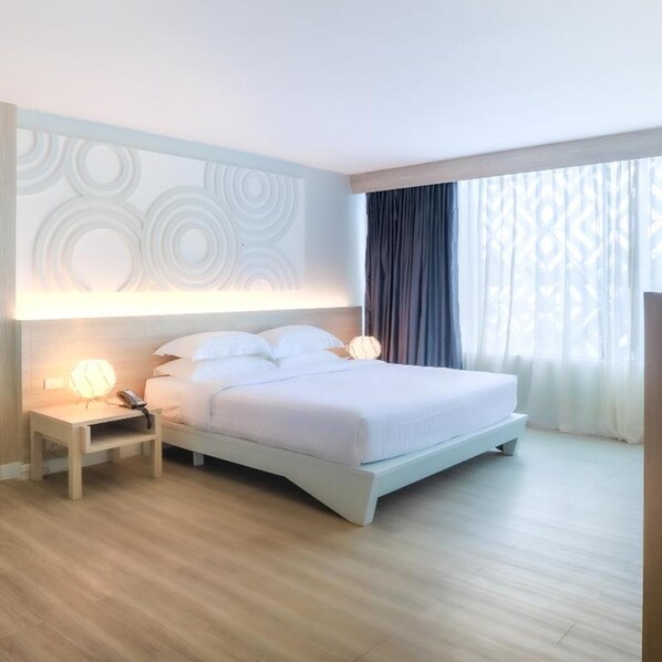 A hotel room with a bed, bedside tables, and a large window with curtains.