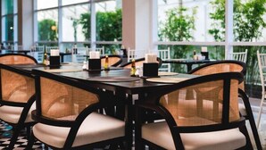 A restaurant with a modern interior, featuring black and white checkered flooring, wicker chairs, and a large window offering a view of greenery outside. - Floral Hotel Chaweng Koh Samui (Koh Samui)