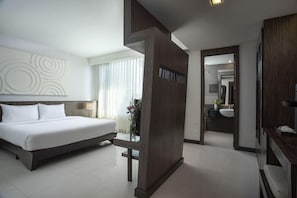 Et moderne hotelværelse med en stor seng, en væg med trædetaljer, et badeværelse med spejl og vask, samt en gang der fører til et andet værelse.