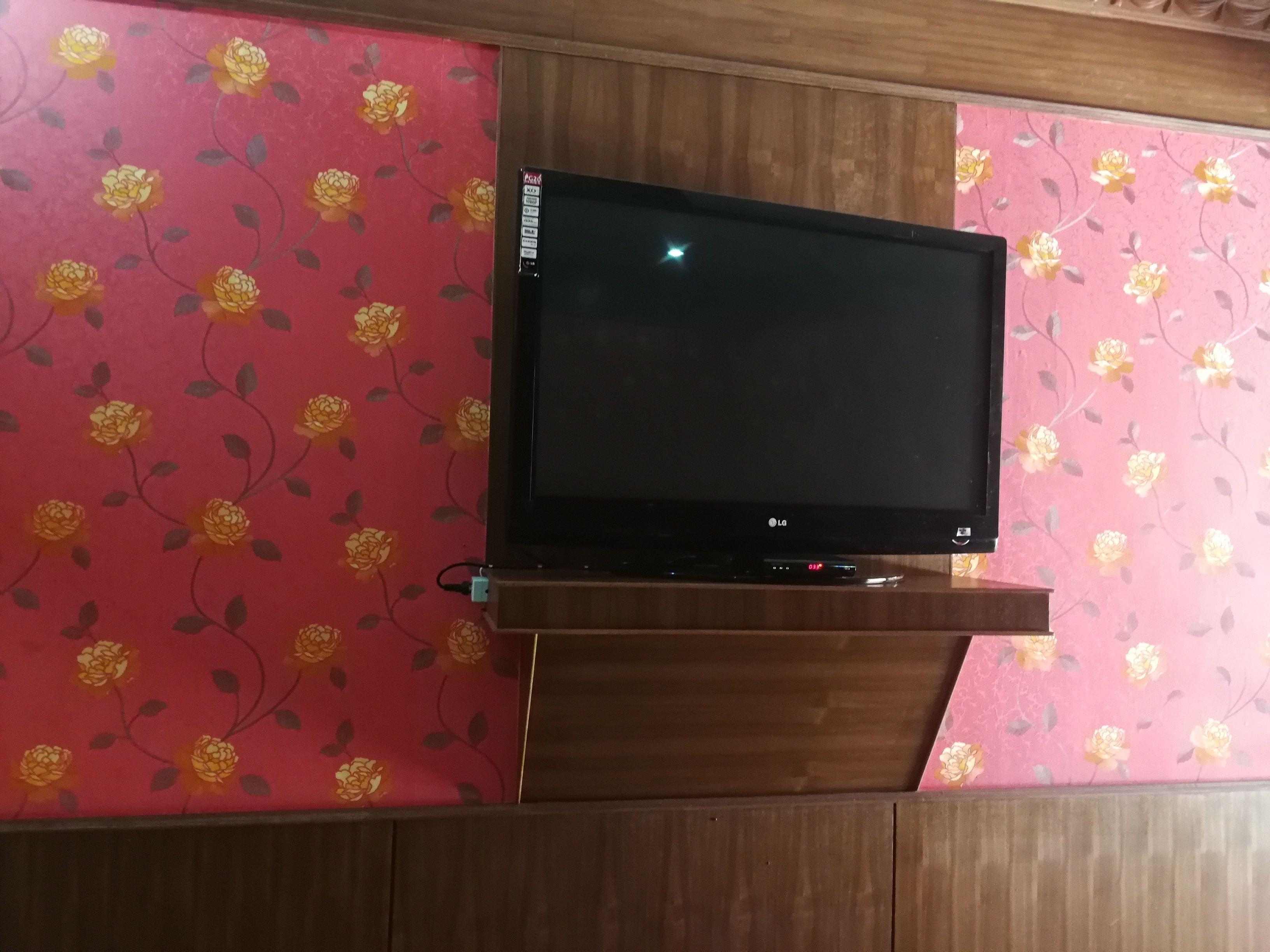 A flat-screen TV mounted on a wooden stand against a wall with floral wallpaper.