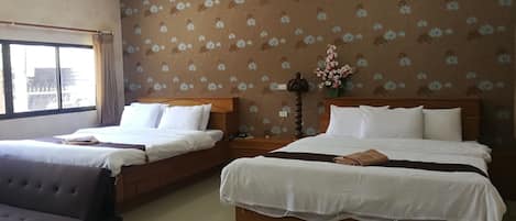A hotel room with two beds, a sofa, a window with curtains, and a floral wallpaper.