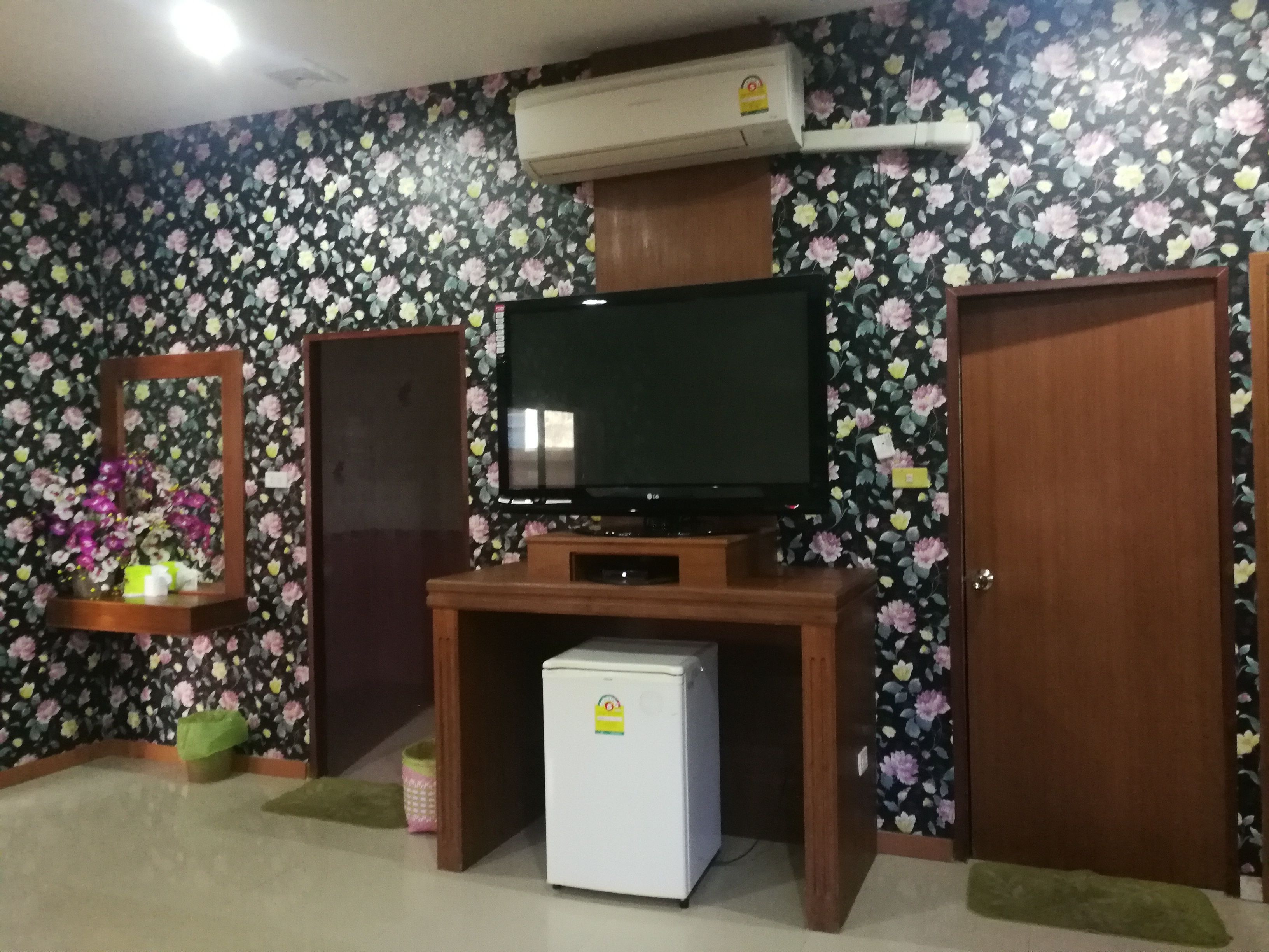 A room with a television on a wooden stand, a small refrigerator, a mirror, and a door.