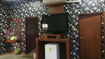 A room with a television on a wooden stand, a small refrigerator, a mirror, and a door.