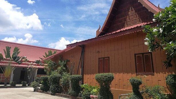 A traditional building with a red tiled roof and a pointed roofline, surrounded by well-maintained greenery. - Reurn Thai Resort Ratchaburi (Damnoen Saduak)