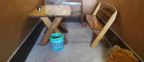 A small, narrow room with a wooden table and two chairs. A blue trash bin is on the floor.