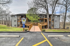 Un bâtiment doté d’un escalier en bois menant à un balcon, un parking délimité par des lignes jaunes et un panneau indiquant les places de stationnement réservées aux personnes handicapées.