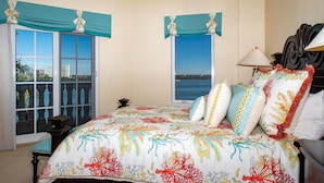 Quarto com cama grande, vista para a água pelas janelas e varanda com vista para a cidade.