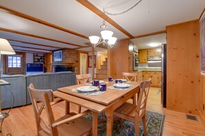 A dining area with a wooden table and chairs, a chandelier, and a kitchen in the background. - North Conway Home: Walk to Cranmore Mtn Resort! (North Conway)