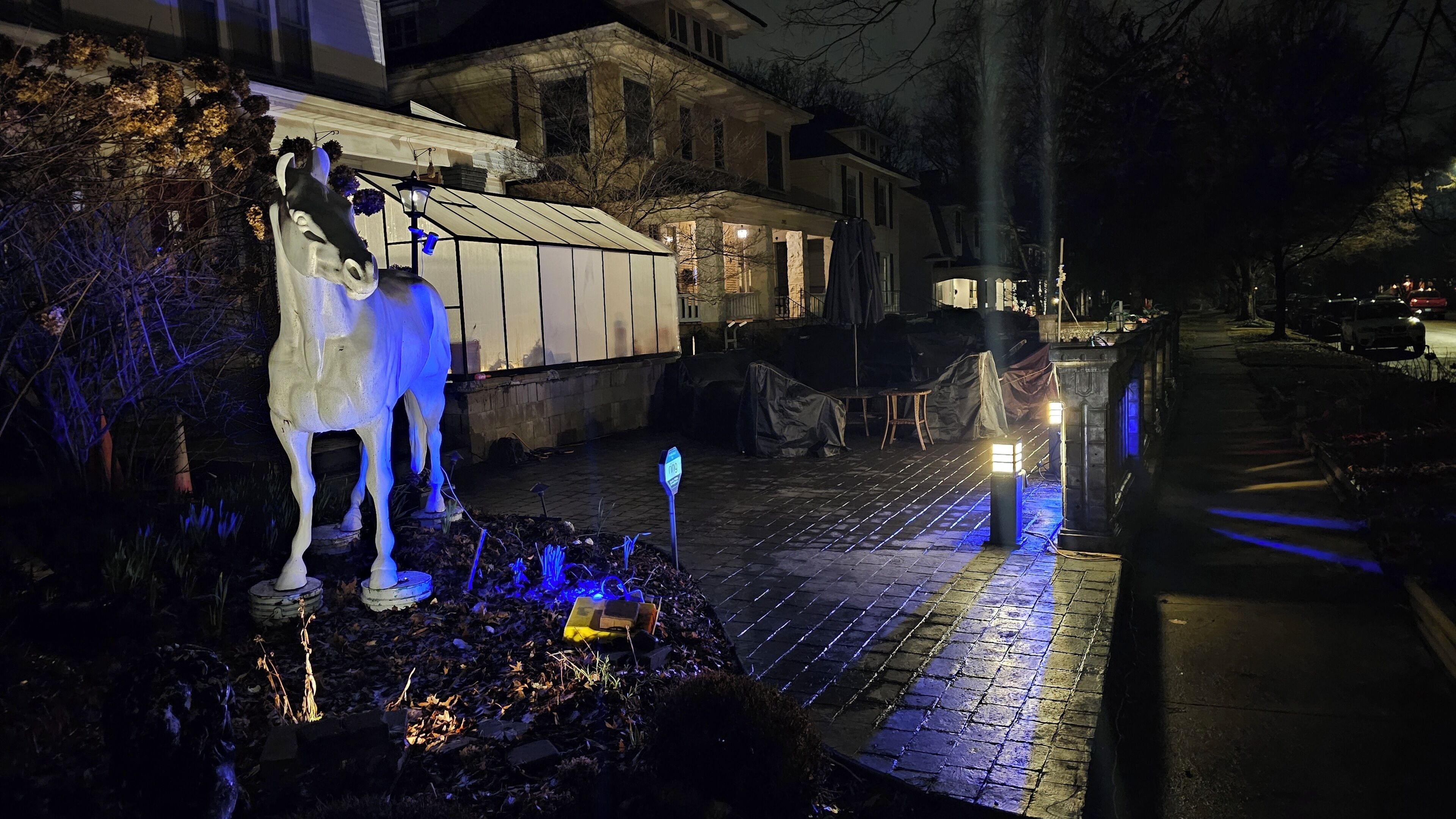A nighttime scene with a horse statue, a covered outdoor area, and a street with parked cars.