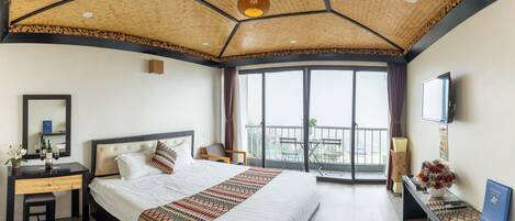 A hotel room with a large bed, a desk, a chair, a TV, and a balcony with a view.