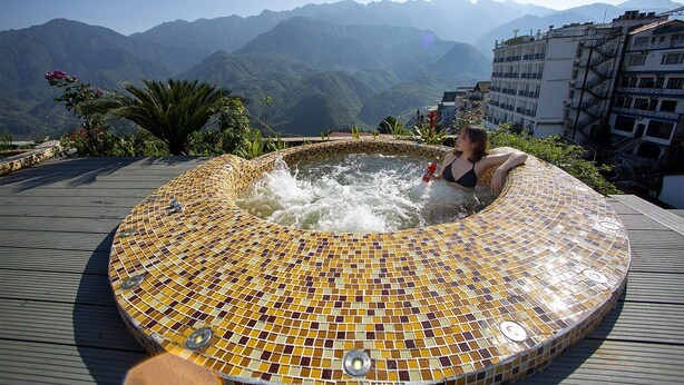 Een vrouw ontspant in een hottub met mozaïektegels, met een bergachtig landschap op de achtergrond.