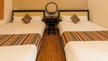 A hotel room with two beds, a nightstand with a mirror, and a patterned rug.