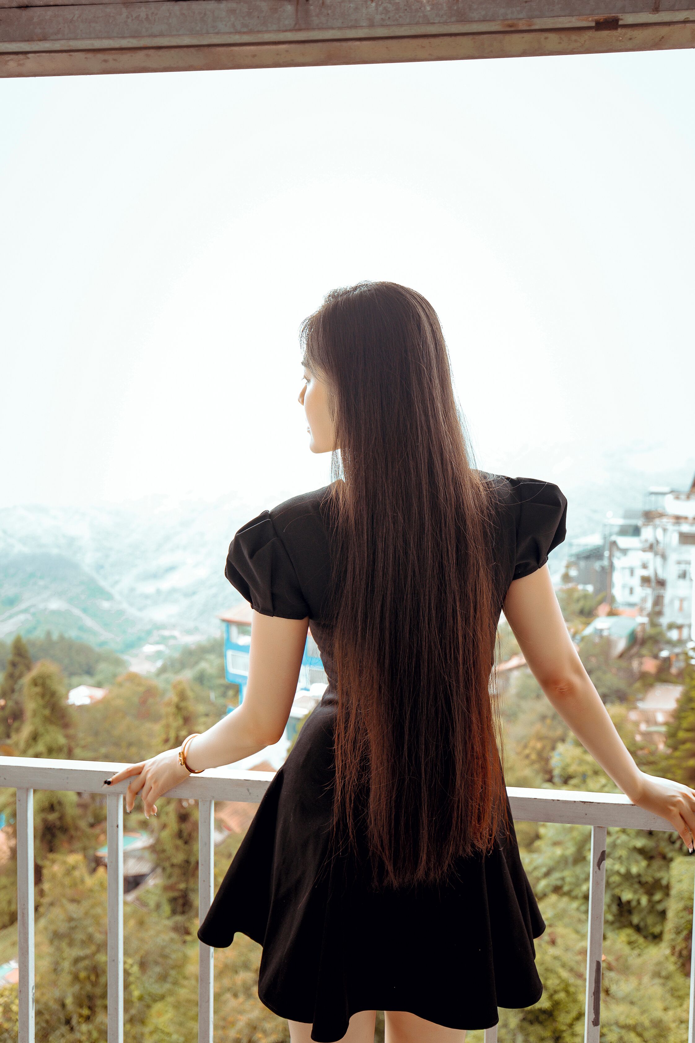 A person standing on a balcony with a view of a mountainous landscape and buildings in the distance.
