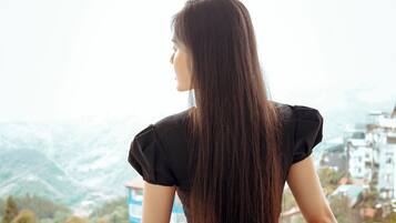 A person standing on a balcony with a view of a mountainous landscape and buildings in the distance.