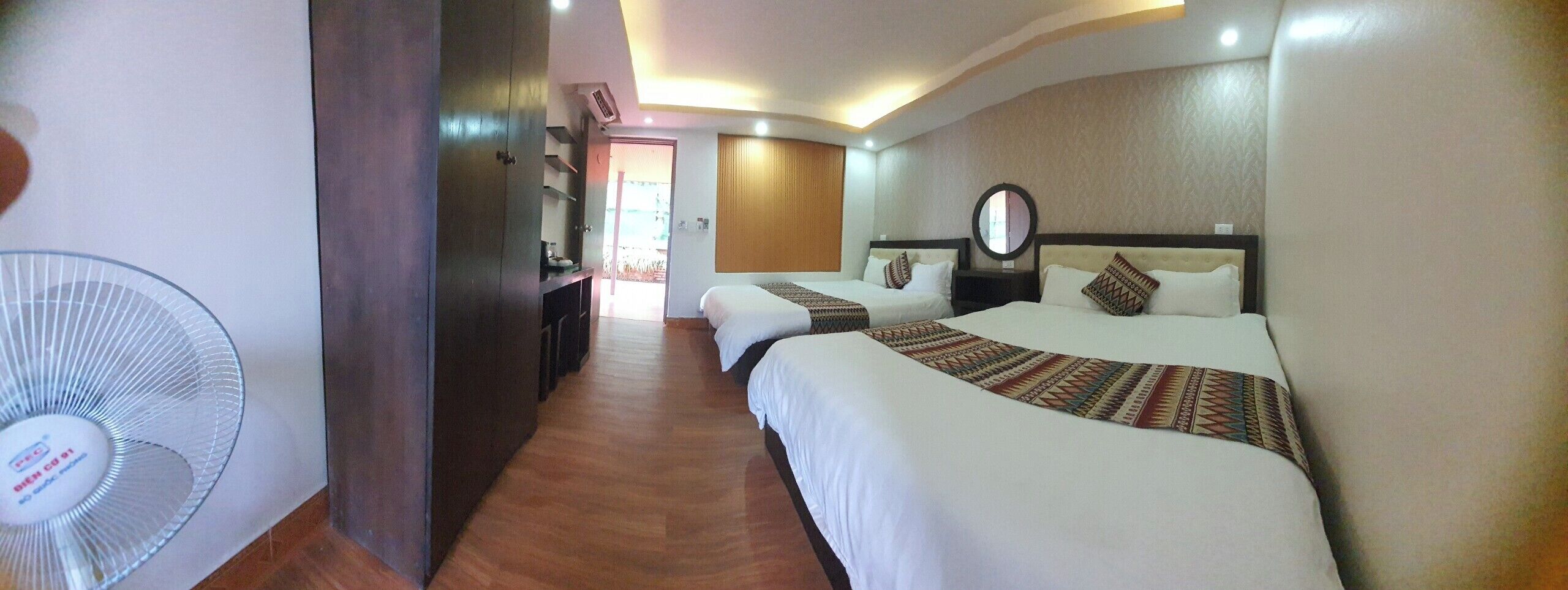 A hotel room with two beds, a large fan, and a wooden floor.