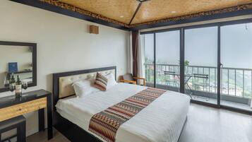Ein Hotelzimmer mit einem großen Bett, einem Holztisch, einem Spiegel und Blick auf die Stadt durch große Fenster.