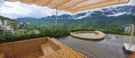 A rooftop terrace with a mosaic-patterned seating area, a small hot tub, and a view of a mountainous landscape.