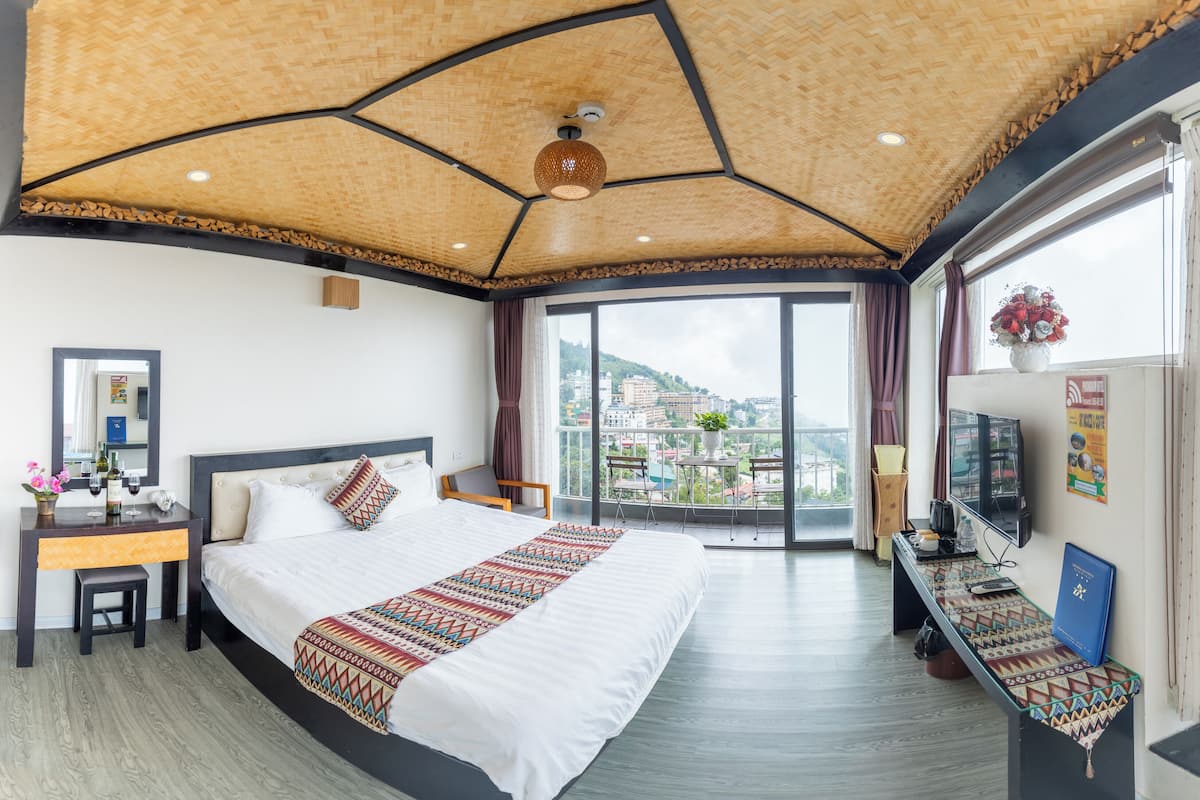 Hotelkamer met een groot bed, een bureau met een computer, een stoel en een balkon met uitzicht op de stad.